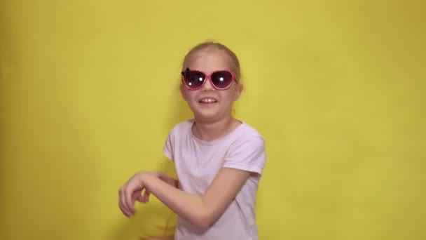 Grappig klein meisje in stijlvolle zonnebril springen en swingende handen terwijl dansen als een konijn tegen een gele achtergrond — Stockvideo