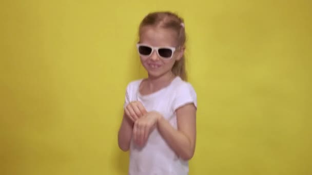 Güneş gözlüklü komik küçük kız sarı arka planda tavşan gibi dans ederken zıplıyor ve el sallıyor. — Stok video