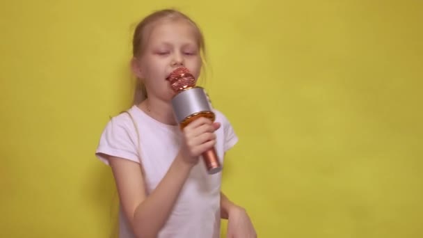 Entzückendes kleines Mädchen mit Hasenohren und Mikrofon, das lächelt und in die Kamera schaut, während es während der Osterfeier vor gelbem Hintergrund Lieder singt — Stockvideo