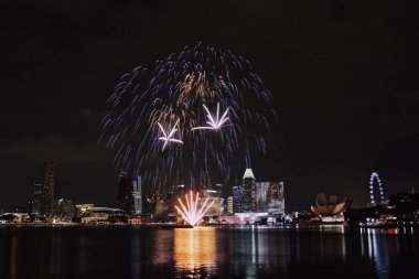 Gece kentinde havai fişekler ve nehirde yansıma