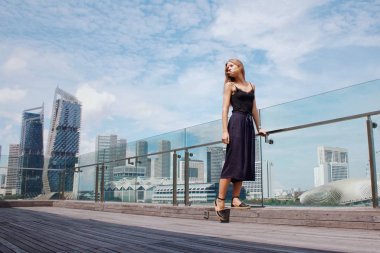 Siyah elbiseli genç kadın şehir geçmişinde poz veriyor.