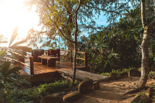 Wooden Terrace in the glory of the sunset at the hill with beautiful view and jungle surrounding. Comfortable seats and wooden table in the canter of terrace.