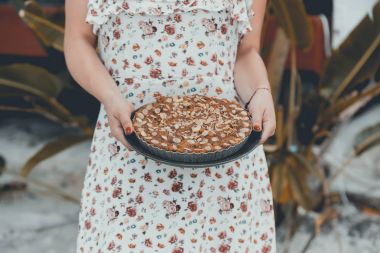 Beyaz elbiseli kadın Muzlu Kek elinde tutar. Pasta badem parçaları görünür üst kısmında.