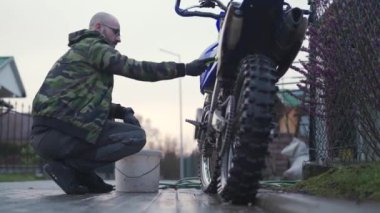 Genç adam motosikleti yarışa hazırlamak için fırça ve hortum kullanarak motokros 'u elle yıkıyor. 4K Görüntü.  