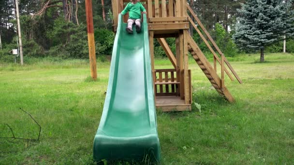 Glückliches Kleinkind rutscht auf Kinderspielplatz im Park ab. — Stockvideo