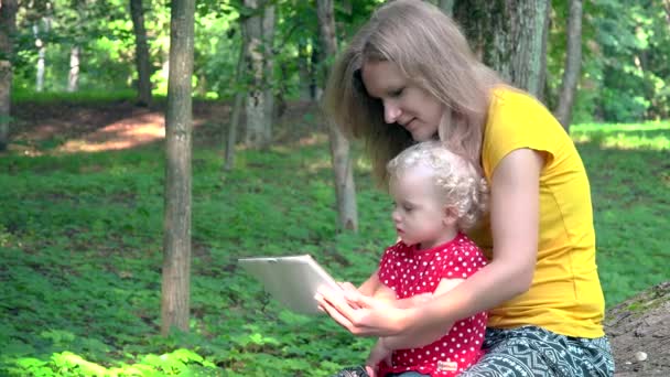 공원에 태블릿 컴퓨터를 사용 하 여 귀여운 딸을 가진 여자. — 비디오