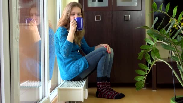 Gelukkige vrouw met warme kleren drinken thee en droom zitten op warme radiator. — Stockvideo