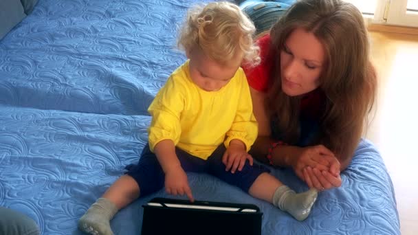 女人和她的女儿小女孩在玩床与平板电脑 — 图库视频影像