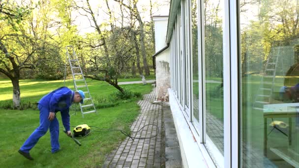 Muž mytí konzervatoři okno s proudem vody odrážející na sklo