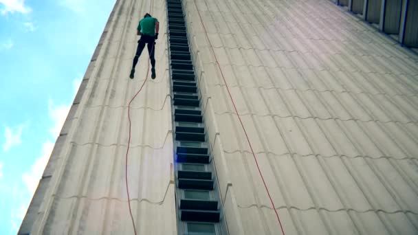 Fearless man descend down with cord on skyscraper wall. Blue cloudy sky — Stock Video