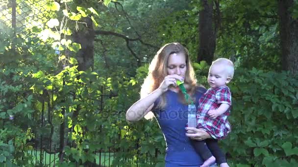 Hübsche blonde Frau pustet Seifenblasen und schöne Baby genießen es in hellem Sonnenlicht. 4k — Stockvideo