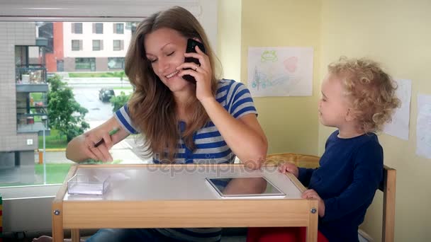 Madre telefono di chiamata e aiutare la bambina a giocare con tablet. Lavoro donna d'affari — Video Stock