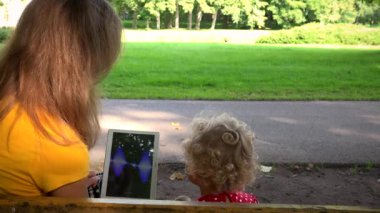 Tablet bilgisayar ile parkta bankta oynarken küçük çocuk kız kadınla