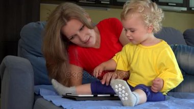Gülümseyen kadın öğretim yürümeye başlayan çocuk kızı yatağa oturmuş tablet PC'yi kullanma.