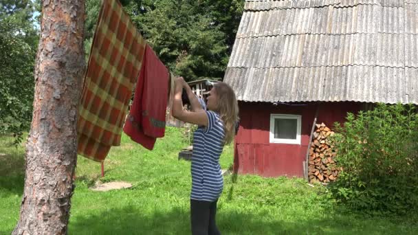 Mujer aldeana colgando ropa lavada en el tendedero de la aldea. 4K — Vídeo de stock