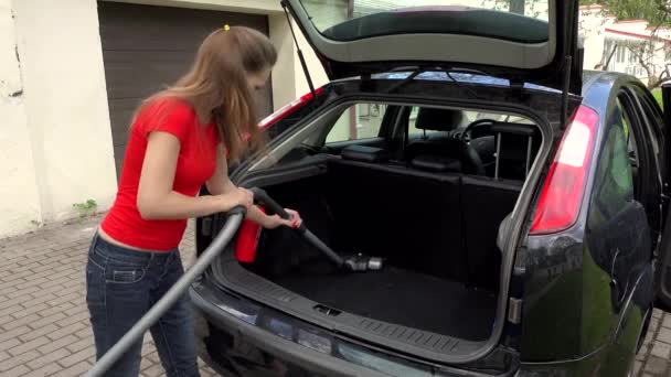 Frau reinigt Kofferraum von Auto mit Staubsauger.