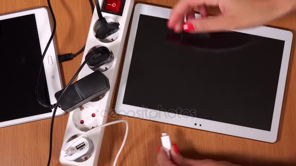 Frauenhände stecken Tablet-Computer und Handys an Ladegeräte in Verlängerungssteckdosen — Stockvideo