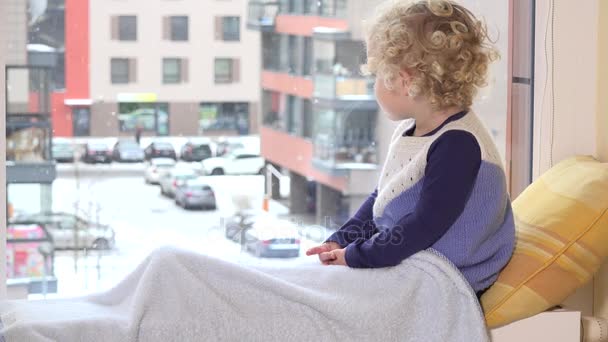 Маленька дівчинка-малюк дивиться з вікна в зимовий день зі сніговим пейзажем — стокове відео