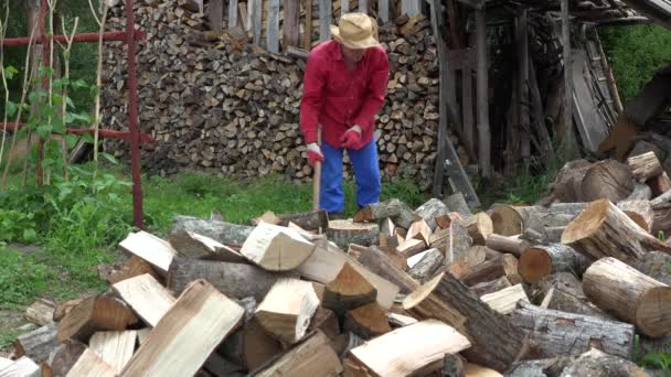 Man met hoed chop brandhout bijl voor de winter. Werken in het land. 4k — Stockvideo