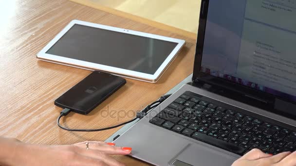 Impiegato utilizzando il computer e cablato ricarica smart phone sul tavolo. primo piano — Video Stock