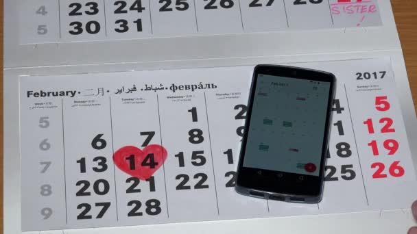 Forma di cuore dipinta su calendario di carta e mano di donna che tocca lo smartphone — Video Stock