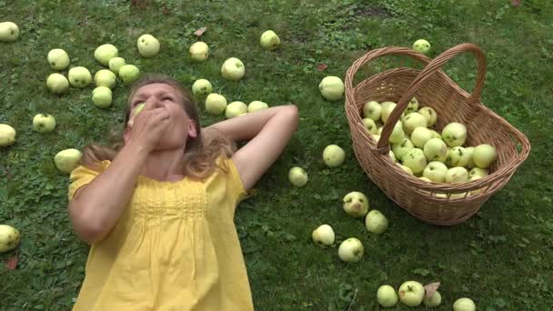 Молода жінка їсть свіже яблуко, що лежить на траві в літньому саду. 4-кілометровий — стокове відео
