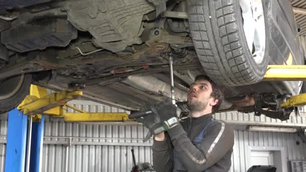 Mecánico automático masculino con llave que trabaja debajo del coche en el garaje — Vídeos de Stock