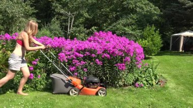 Seksi kadın kırmızı çiçek yatak çevresinde benzinli çim biçme makinesi ile çim keser. 4k