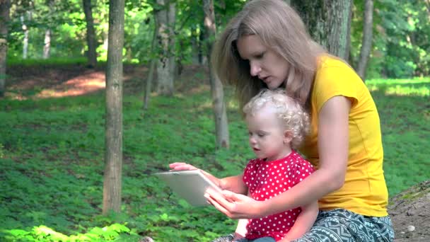 Няня с милой девочкой с помощью планшетного компьютера в парке . — стоковое видео