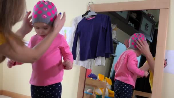 Kvinna och flicka sätta hattar på huvudet nära spegel — Stockvideo