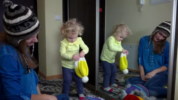 Грайливі сімейні дівчата вимірюють теплі зимові капелюхи біля дзеркала — стокове відео