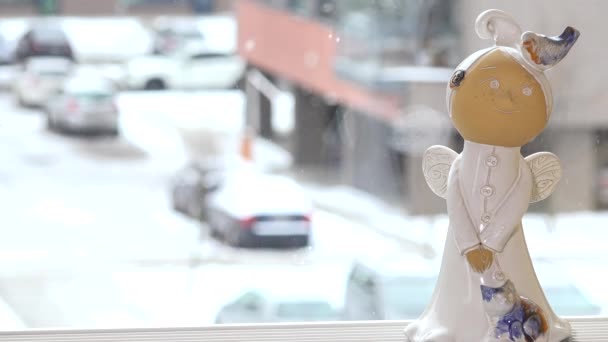 Keramiska ängel staty stående på fönsterbrädan och snö som faller utanför — Stockvideo