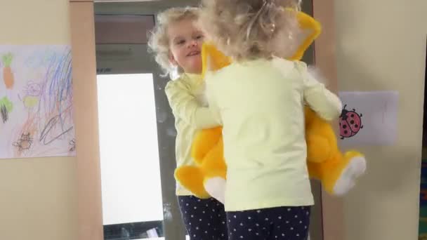 Счастливая девушка с большим плюшевым кроликом позирует перед зеркалом дома — стоковое видео