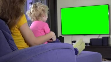 Genç anne ile kızı kızı koltukta dinlenmek ve tv izlemek. Yeşil ekran