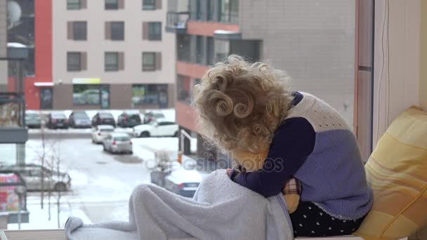 Enfant avec le meilleur ami ours en peluche caresse et baiser en regardant la neige tomber blizzard — Video