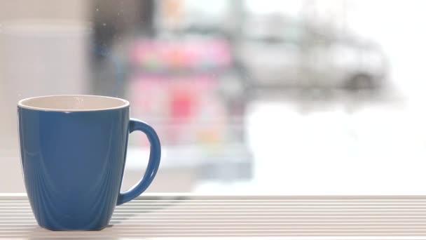 Blue cup of coffee tea hot drink stand on window sill and snow fall outdoor — Stock Video