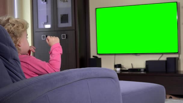 Niño sentado frente a una televisión y ver un programa de niños en. Pantalla clave de croma verde — Vídeo de stock