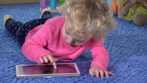 Schattig klein meisje op de maag liggen en gebruik van tablet pc — Stockvideo