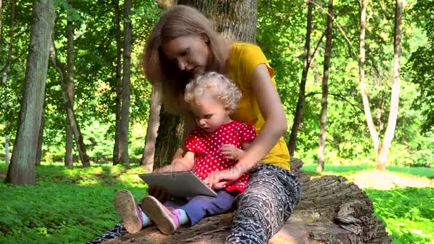 Mamma med barn dotter girl med tablett dator sit på fallna trädstam — Stockvideo