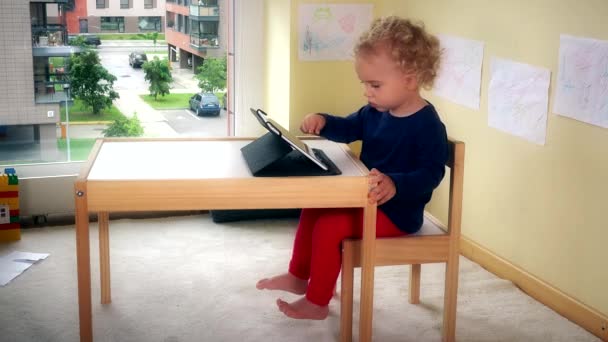 Mooie jongen spelen met tablet pc zittend op een stoeltje in de buurt van tabel. — Stockvideo