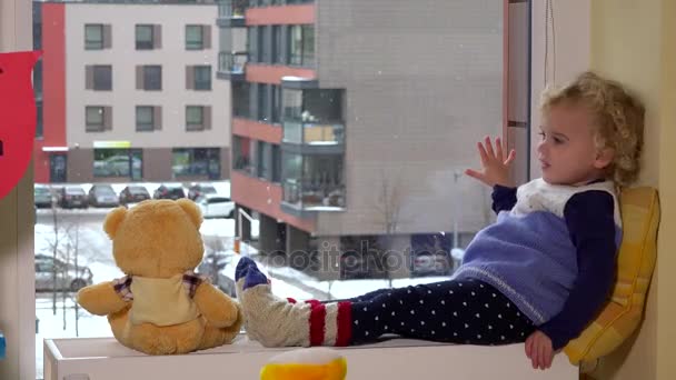 Lindo niño con el mejor amigo oso de peluche sentado cerca de la ventana. Caída de nieve — Vídeos de Stock