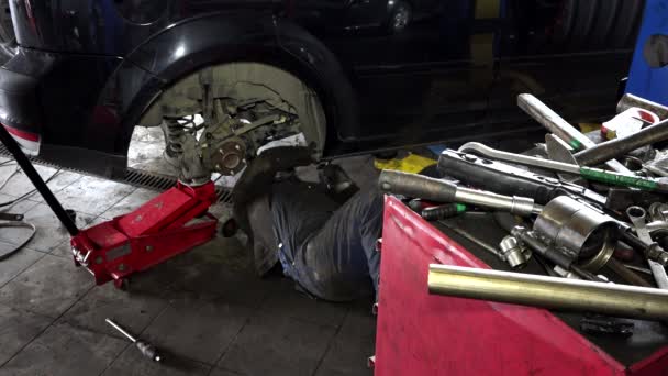 Sujo homem deitado e trabalhando sob carro na garagem de reparação — Vídeo de Stock