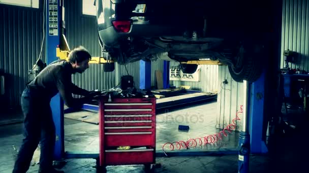 Mekaniker push röd verktyg rutan under upplyft bil. — Stockvideo