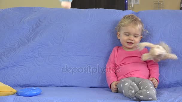 Mjuka leksaker regn faller på Söt blond flicka sitter på soffan. Barn dröm gick i uppfyllelse — Stockvideo