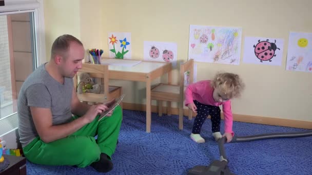 Vader met Tablet PC- en schattig meisje hoover vloer met stofzuiger thuis — Stockvideo