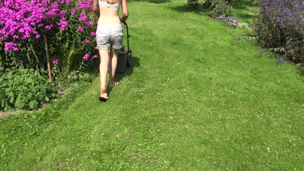 Młoda kobieta w stoczni pchanie kosiarki do trawy przycinanie trawy. 4k — Wideo stockowe