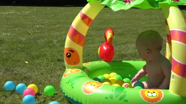 Γελώντας βρέφος μωρό ψεκασμό νερού στην πισίνα γεμάτο πολύχρωμες μπάλες. 4k — Αρχείο Βίντεο