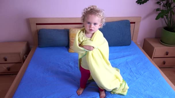 Babymeisje springen op bed verpakt in plaid. — Stockvideo