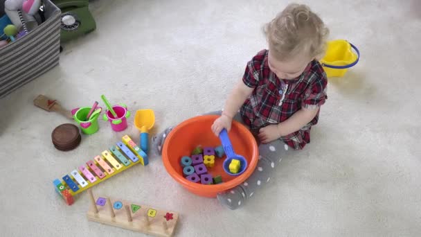 Bebé niña mezclar ladrillos de madera en un tazón con cuchara grande. Imitación de cocina con juguetes — Vídeo de stock