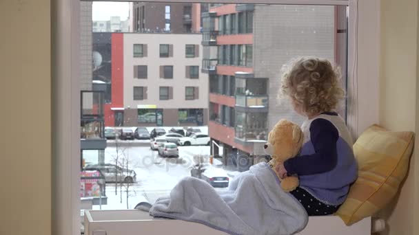 Smutny toddler chłopiec z najlepszy przyjaciel Miś patrząc na śniegu wpadają przez okno — Wideo stockowe
